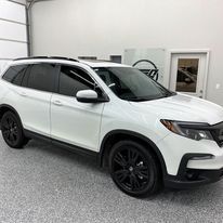A white honda pilot is parked in a garage.
