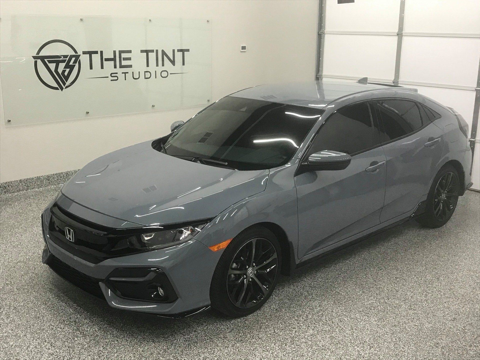 A gray car is parked in a garage next to a sign that says the tint studio.