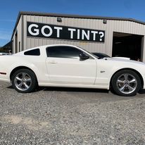 A white mustang is parked in front of a building that says `` got tint ''.