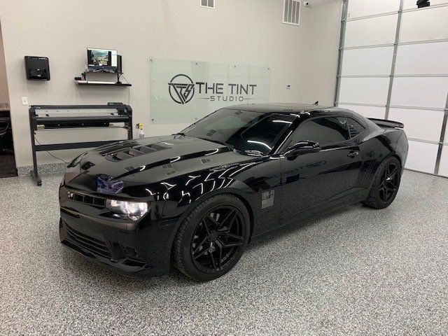 A black car is parked in a garage next to a sign that says the tint studio.