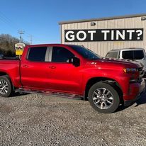A red truck is parked in front of a building that says `` got tint ''.