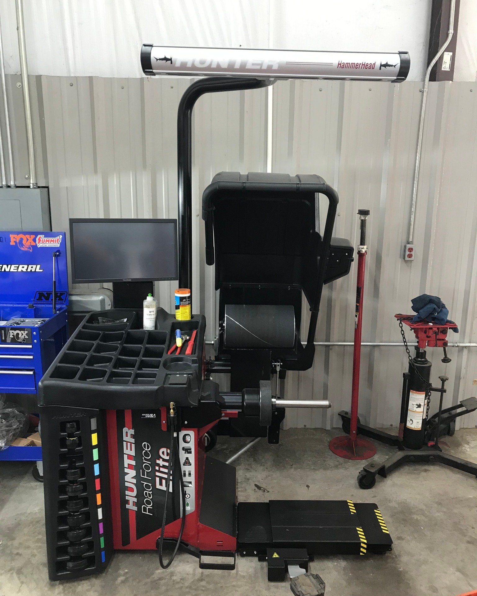 A tire balancing machine is sitting in a garage next to a computer.