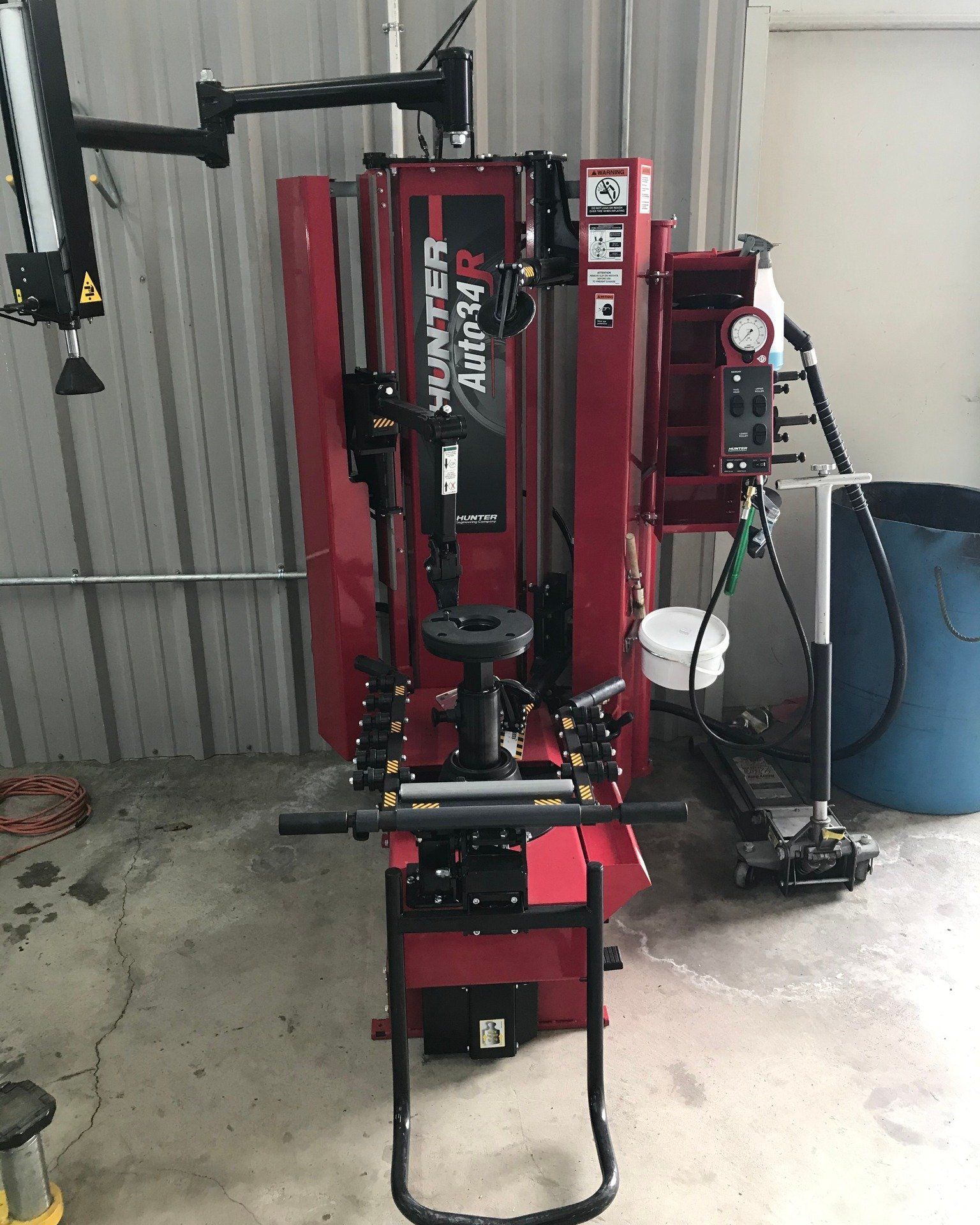 A red tire changer is sitting in a garage next to a blue trash can.