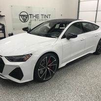 A white car is parked in a garage next to a sign that says the tint studio.