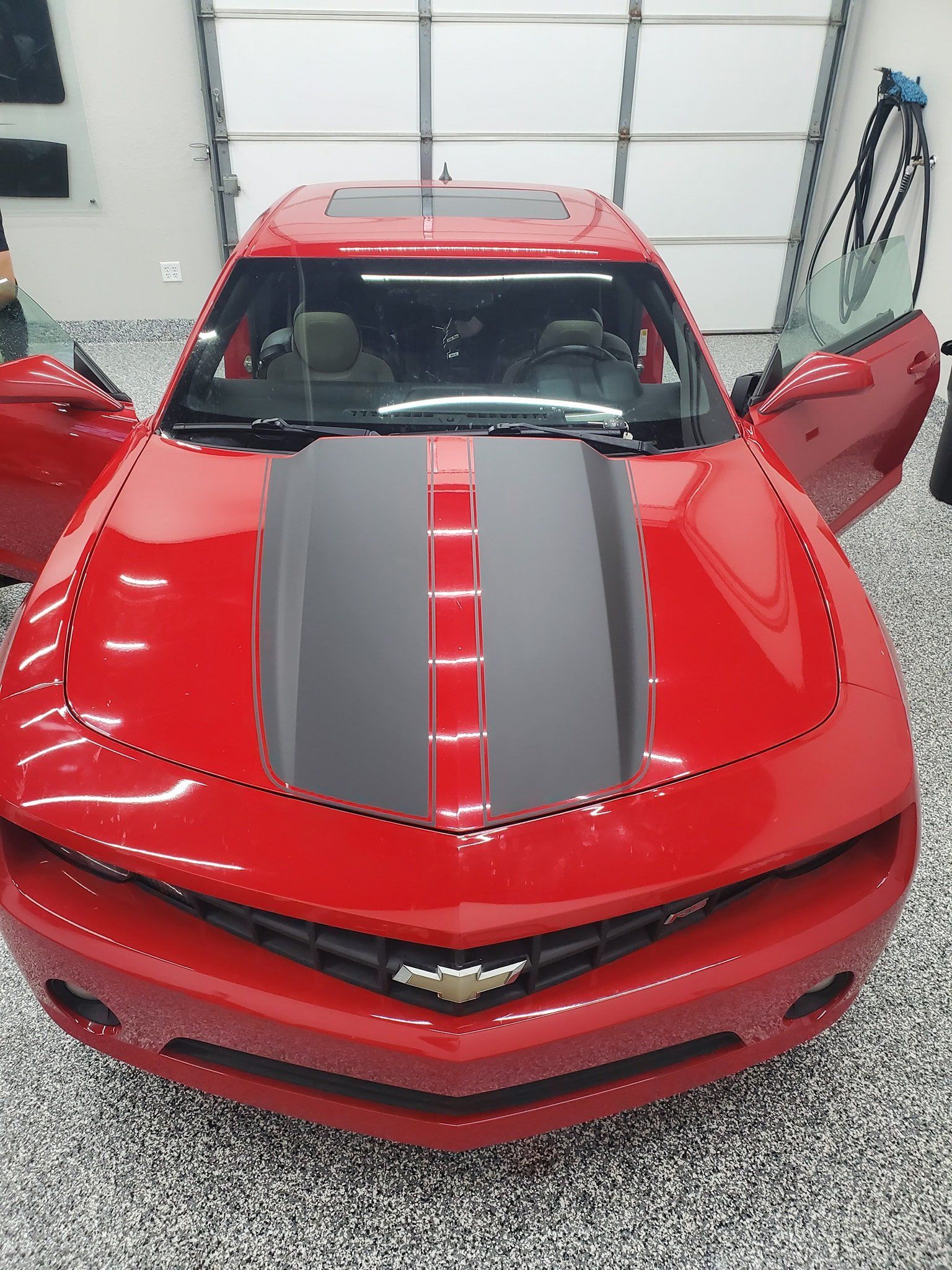 A red car with a black stripe on the hood is parked in a garage.
