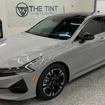 A gray car is parked in a garage next to a sign that says the tint studio.