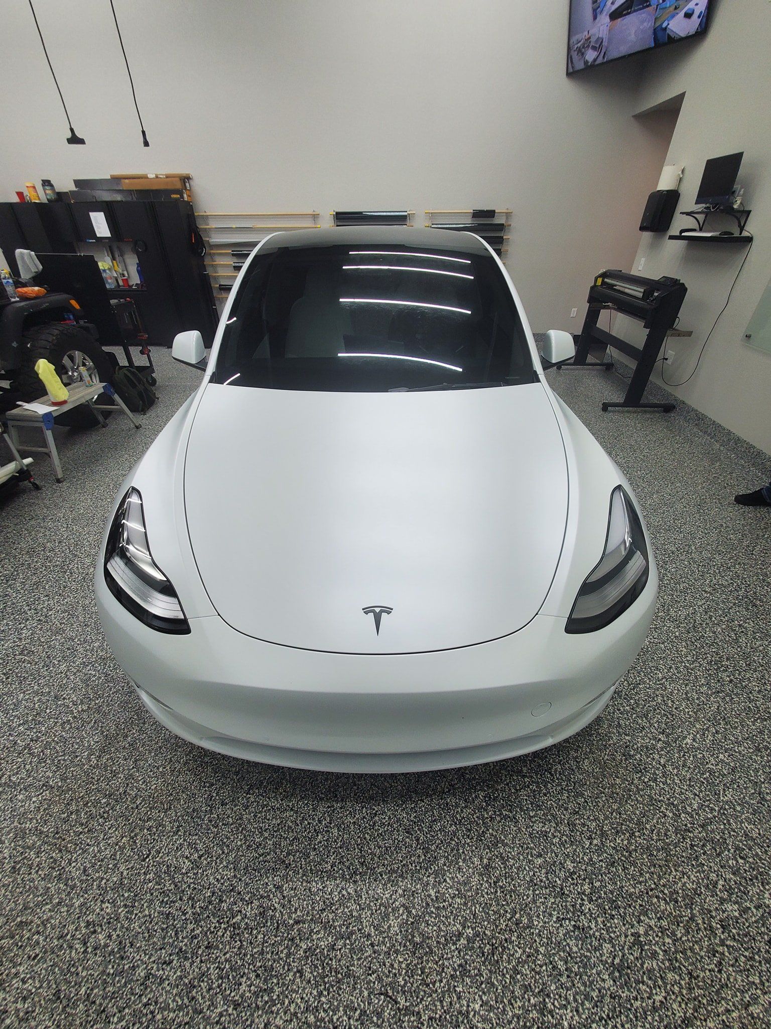 A white tesla model 3 is parked in a garage.