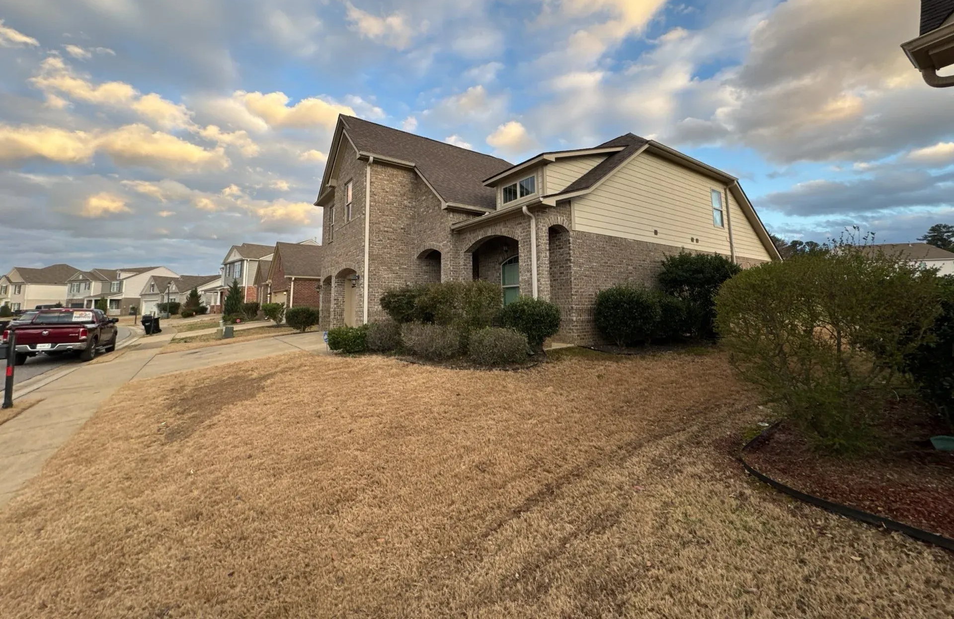 Brick house with brown roof and dry grass lawn on a cloudy day.