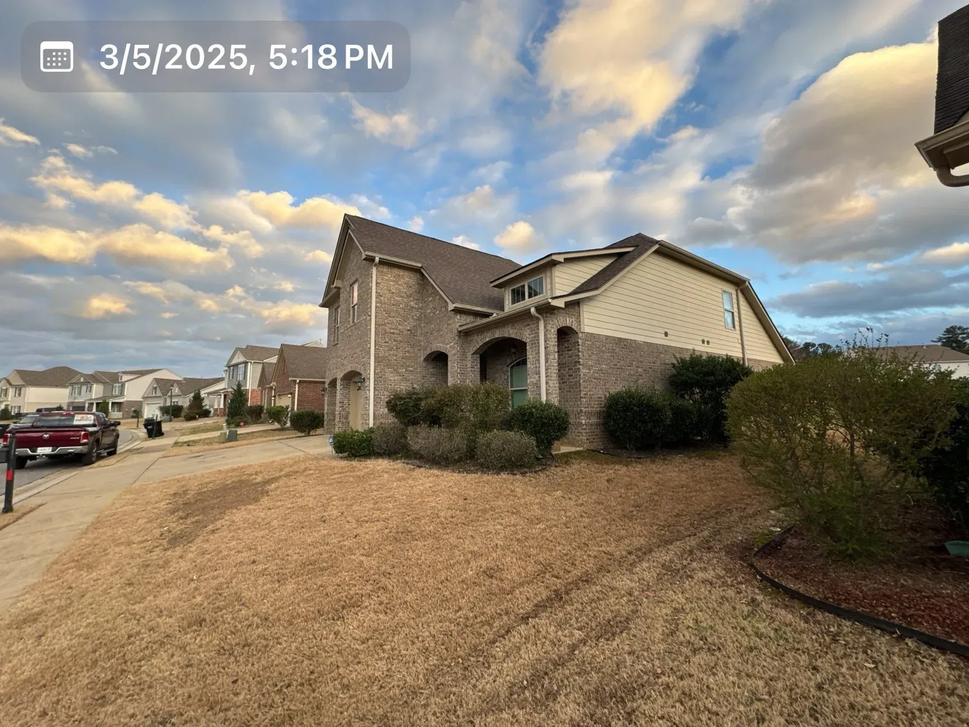 House with brick and tan siding on a cloudy day. Dry brown lawn in the foreground.