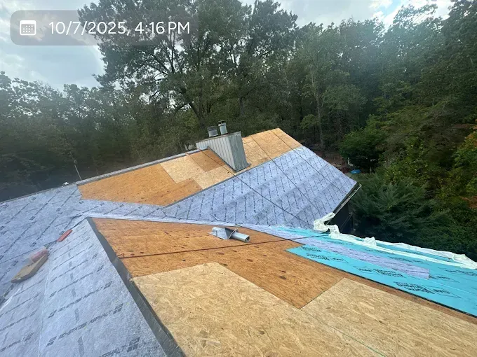 Roof being repaired: plywood, underlayment, and exposed shingles against a backdrop of trees.