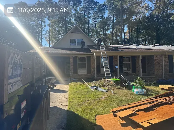 Roofers on a house with a ladder.  A construction dumpster is visible in the yard.