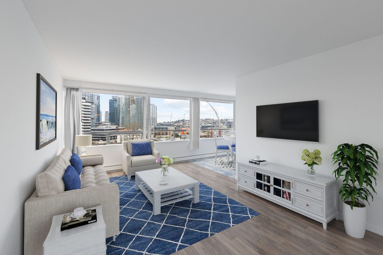 Living room with city view, featuring a blue rug, white furniture, and a mounted TV.