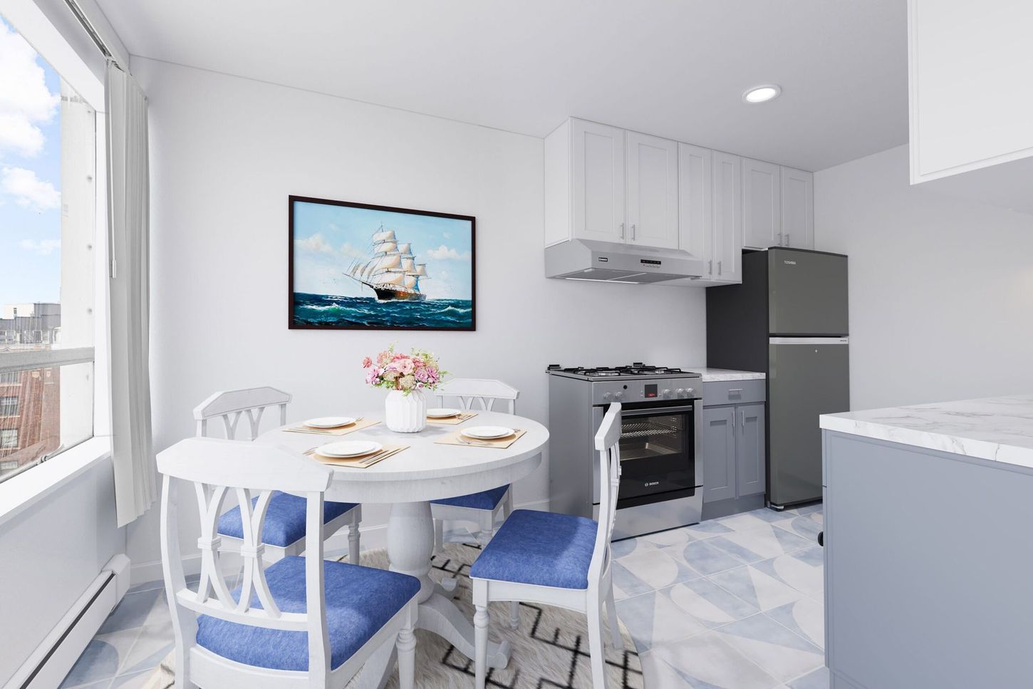 Small white kitchen with round table and chairs, a ship painting, and gray appliances.