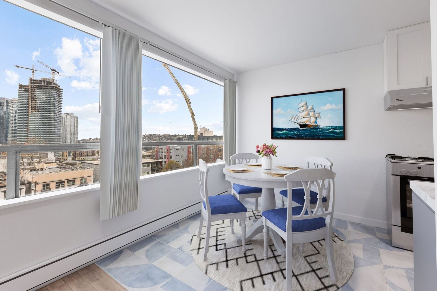 Dining area with city view, round table, blue chairs, and artwork; white walls, rug.