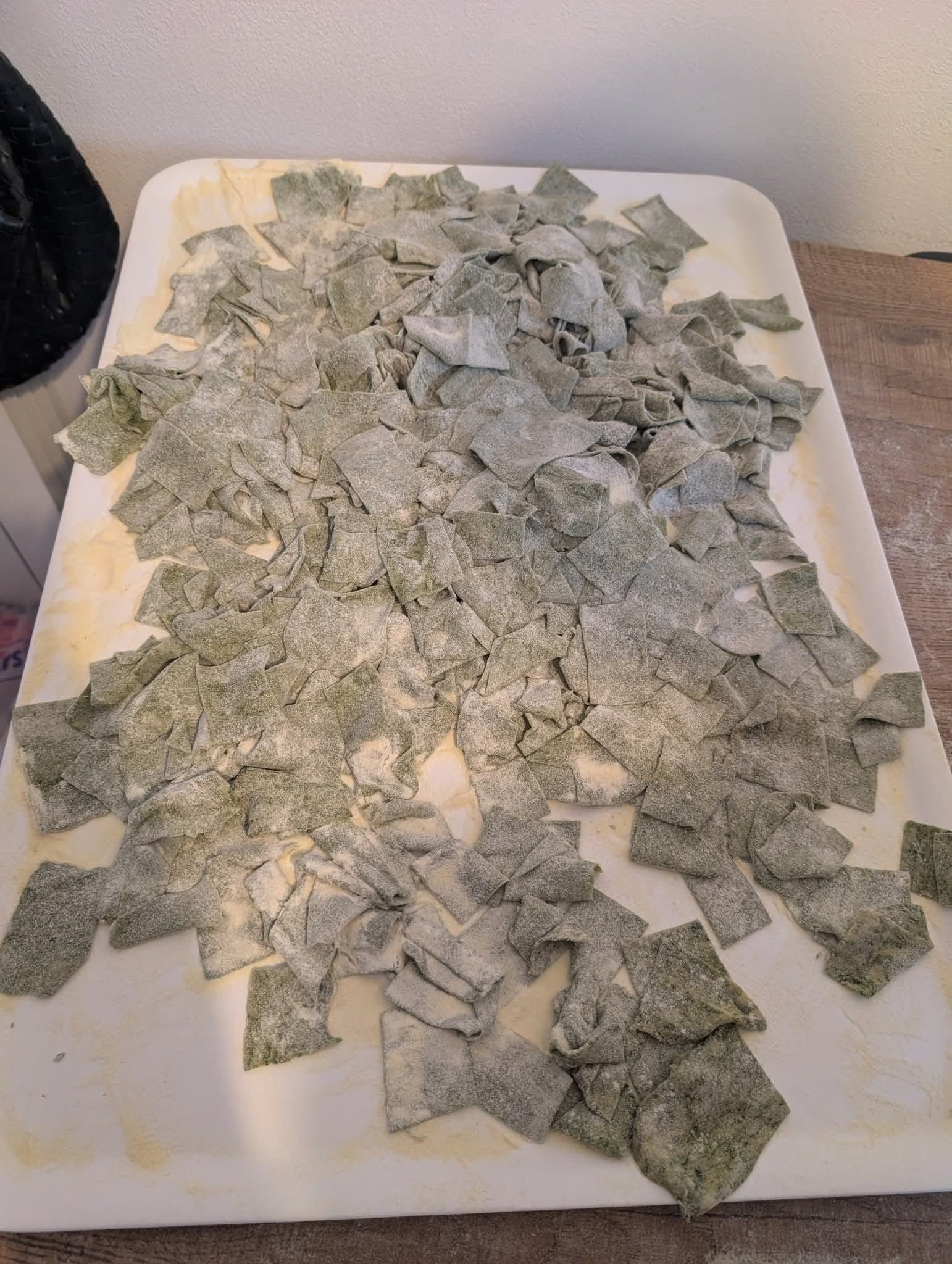 Un vassoio bianco colmo di tanti piccoli pezzi quadrati di pasta verde fatta in casa, cosparsi di farina.