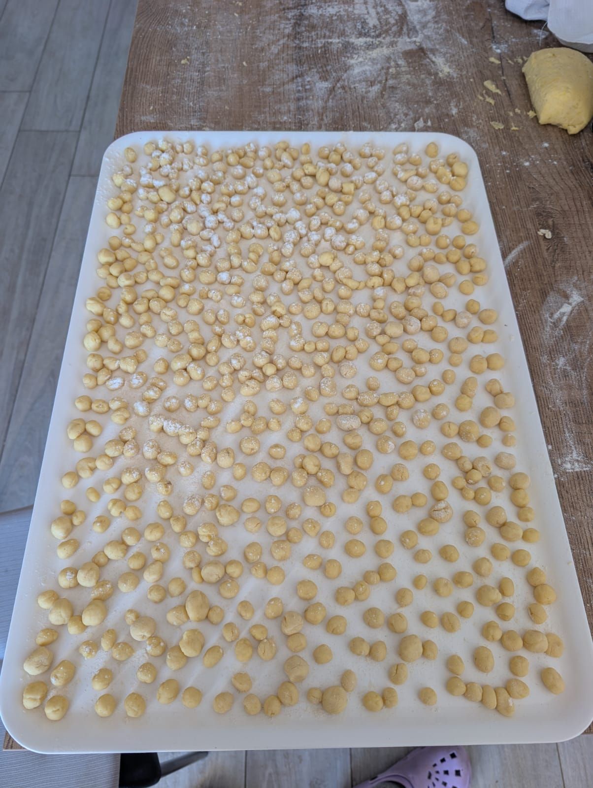 Un grande vassoio rettangolare su un tavolo di legno ricoperto da centinaia di piccoli gnocchi appena fatti e infarinati.