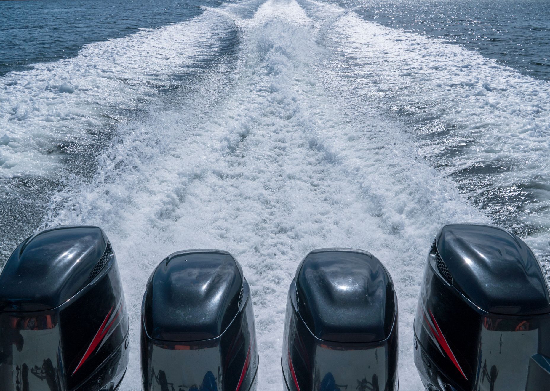 Quattro motori neri di barche agitano l'acqua, creando una scia schiumosa dietro l'imbarcazione.