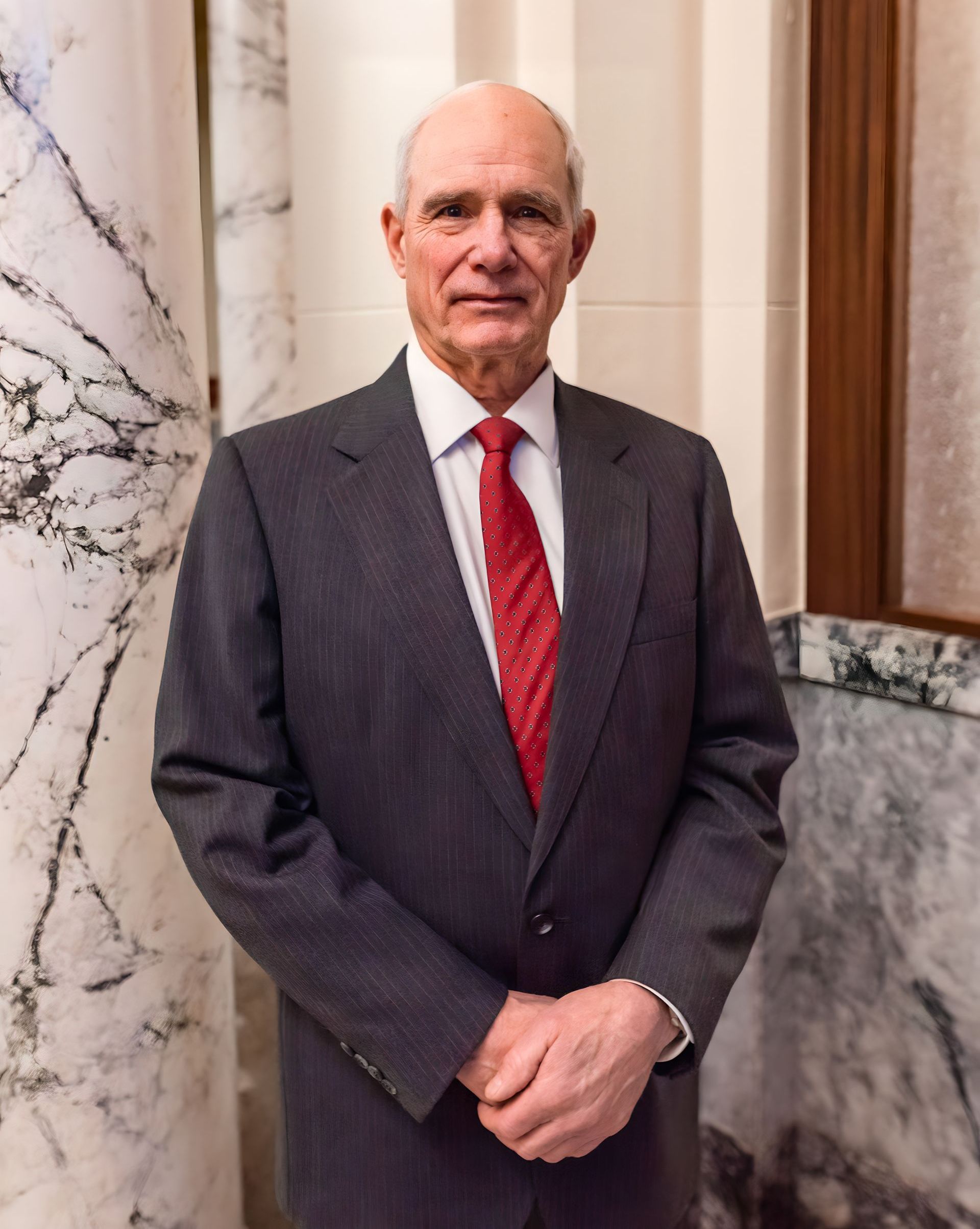 A man in a suit and tie is standing in front of a marble wall.