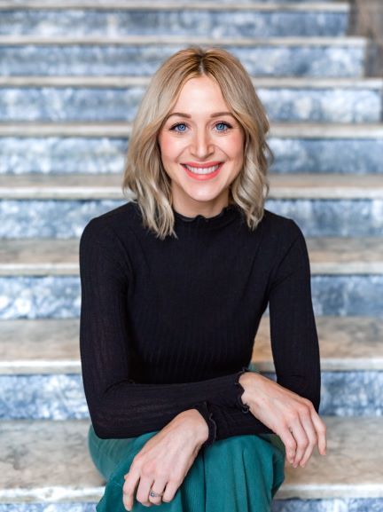 A woman in a black sweater and green skirt is sitting on a set of stairs .