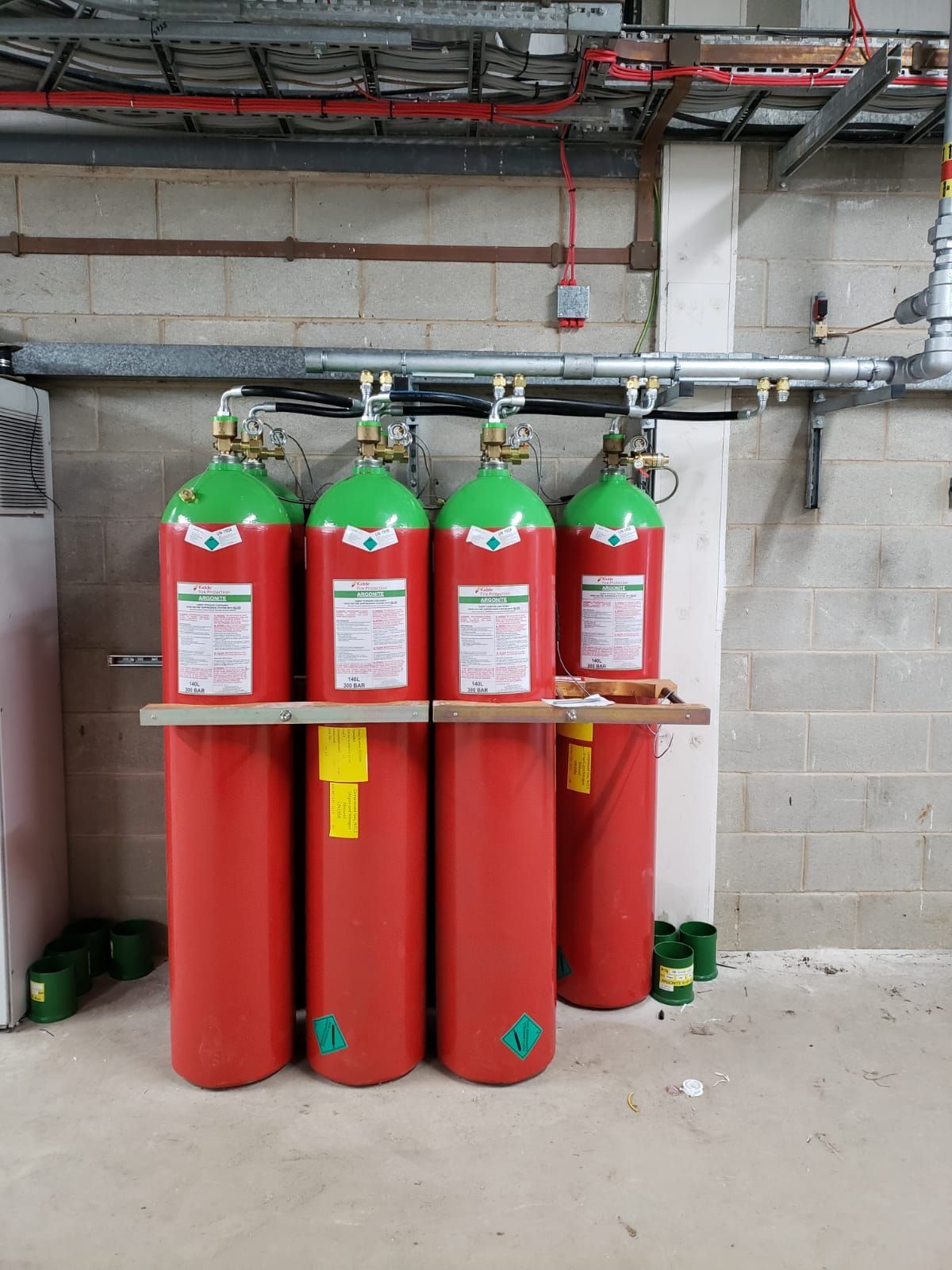 A row of red and green gas cylinders are lined up in a room.