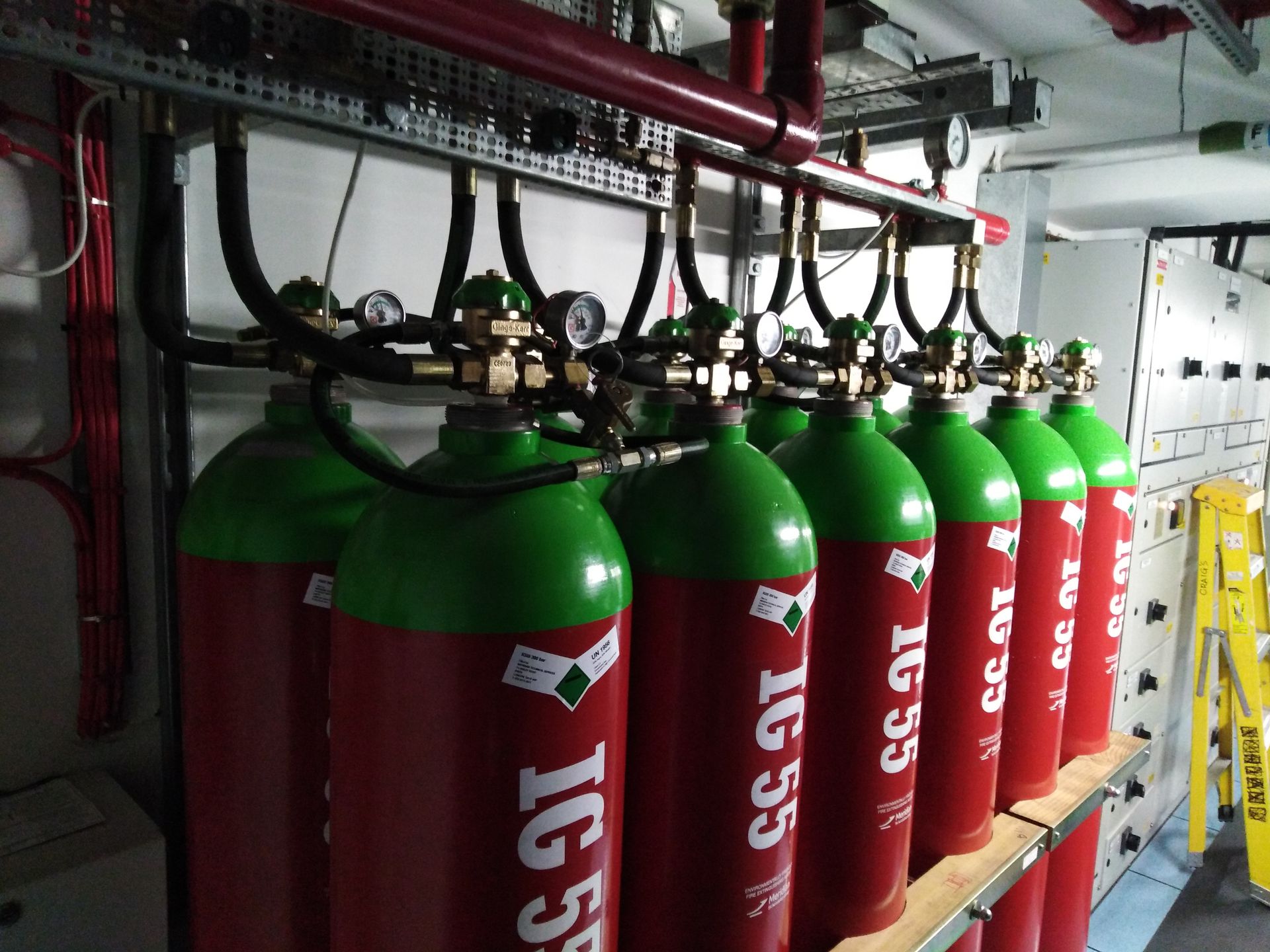 A row of red and green gas cylinders are lined up on a shelf.