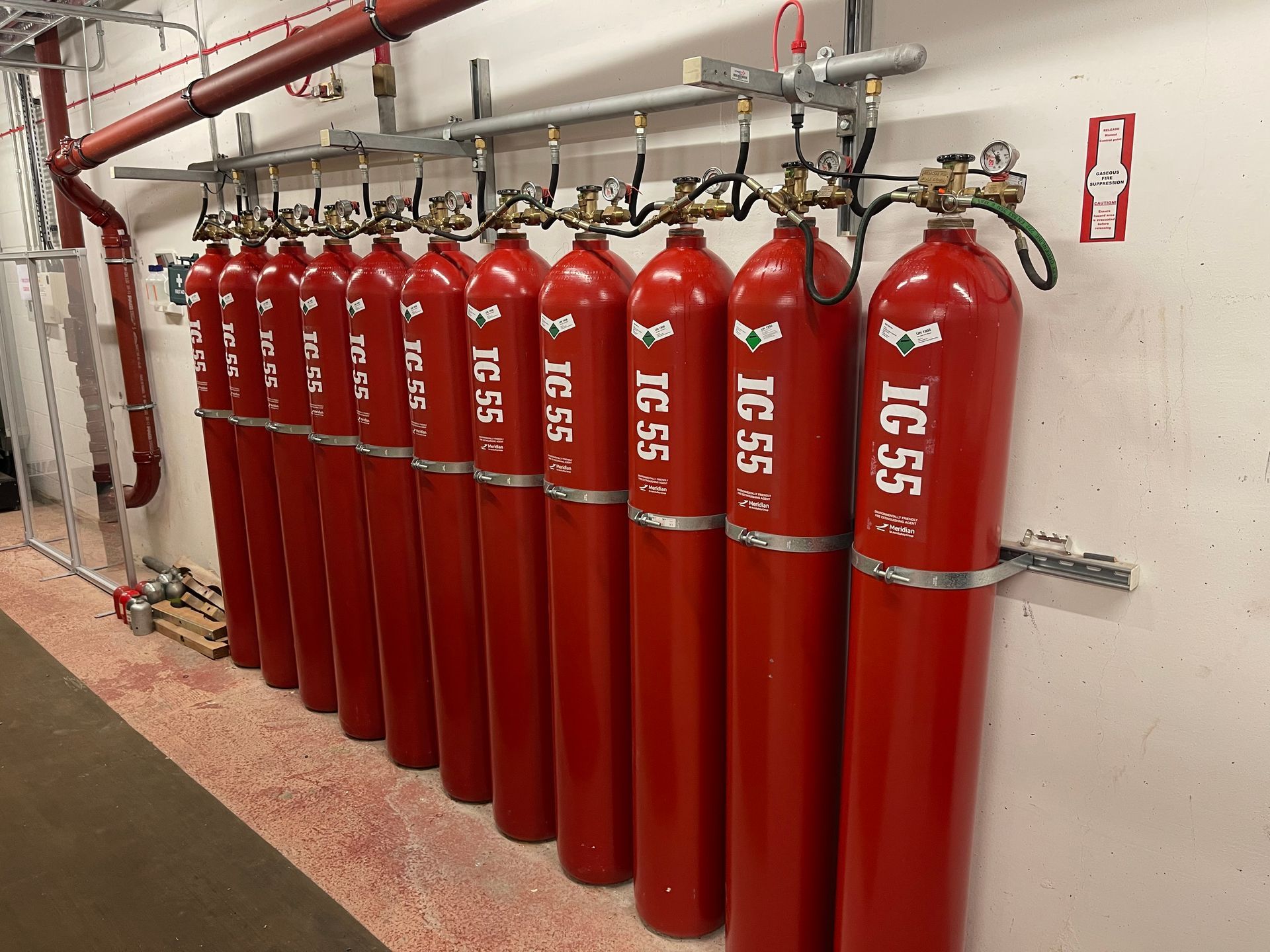 A row of red gas cylinders are lined up on a wall.