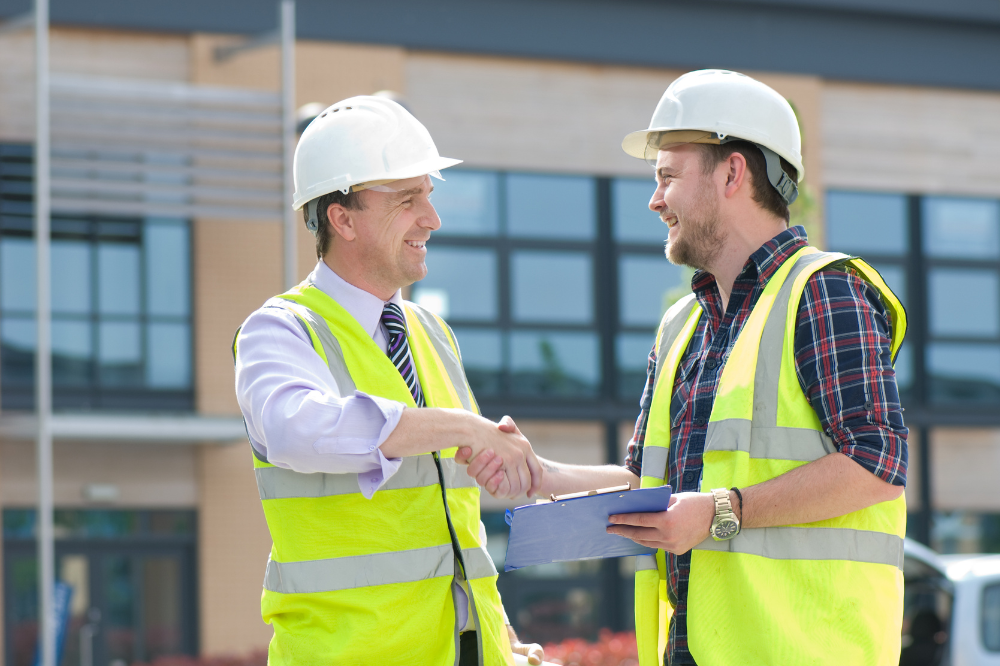 Two construction workers are shaking hands on a construction site.