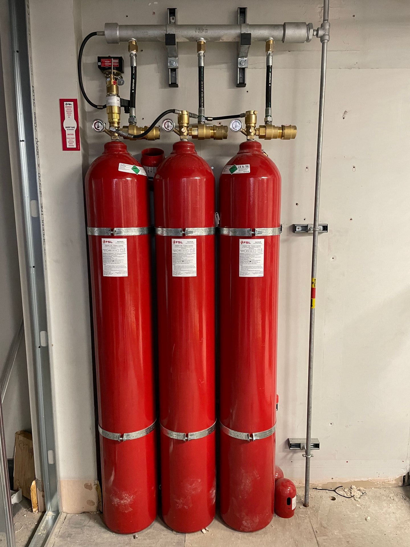 Three red gas cylinders are sitting next to each other on a wall.