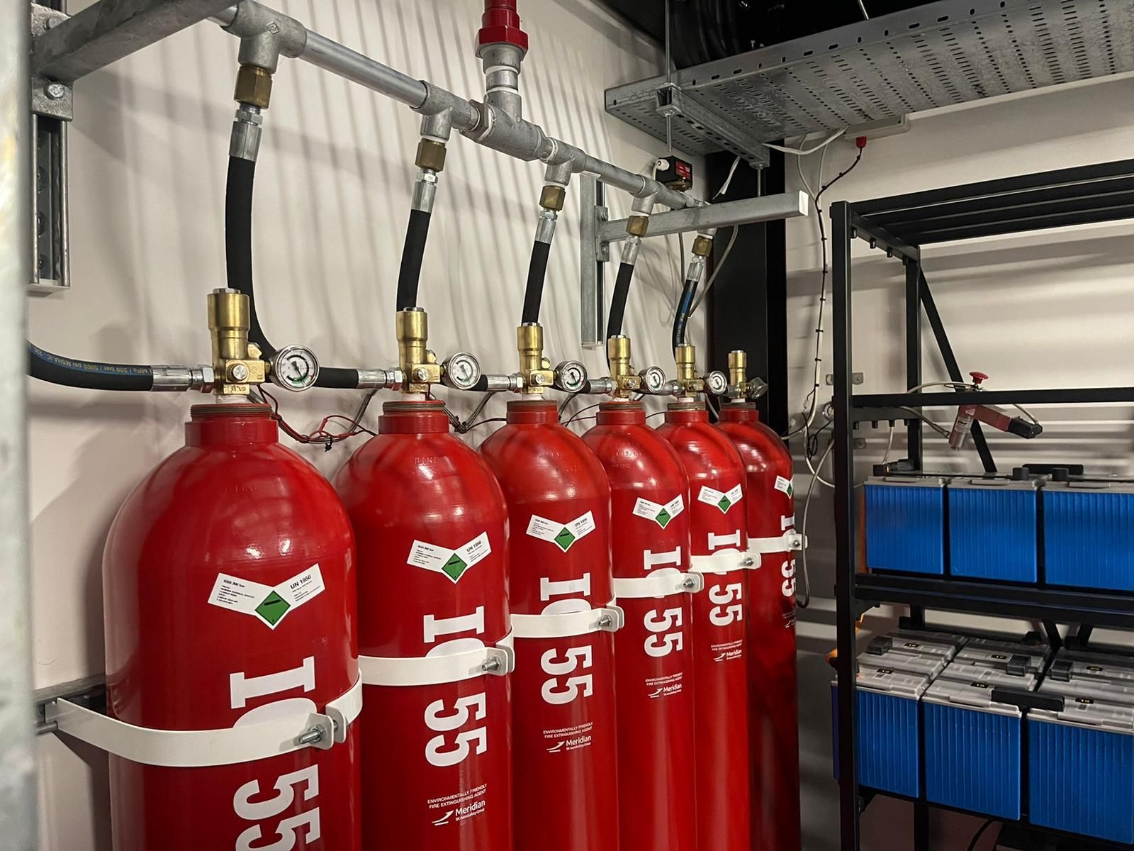 A row of red gas cylinders are lined up on a wall.