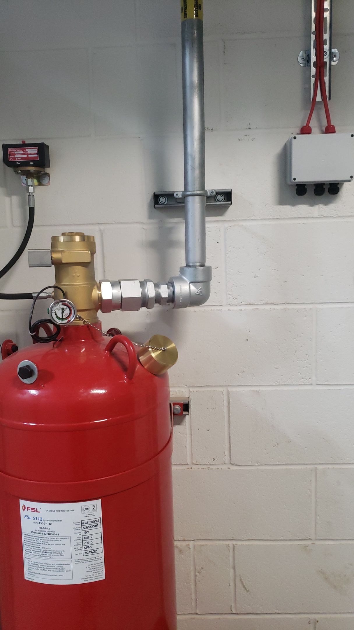A red tank is sitting next to a white brick wall.