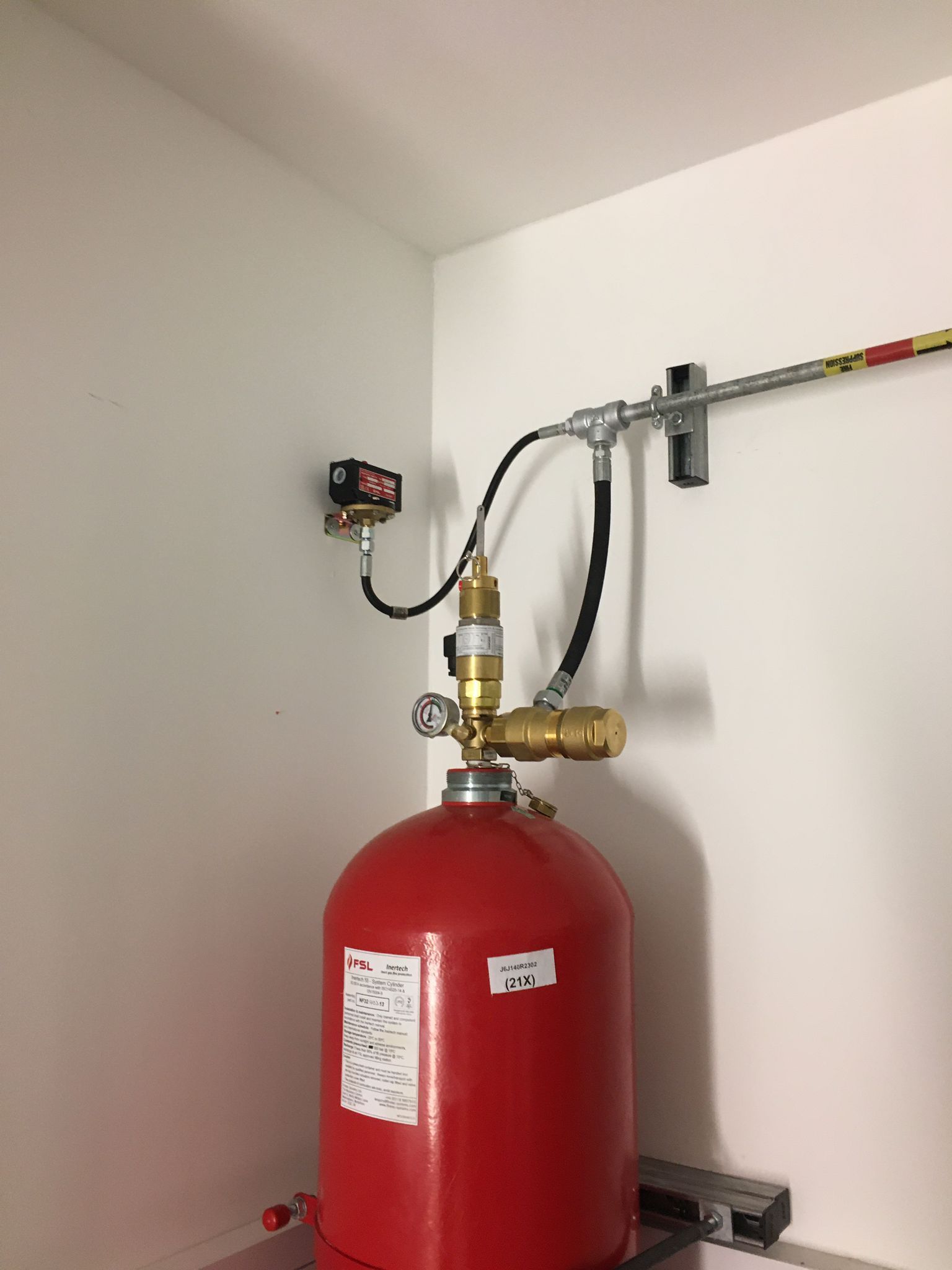 A red cylinder with a hose attached to it is sitting in a corner of a room.
