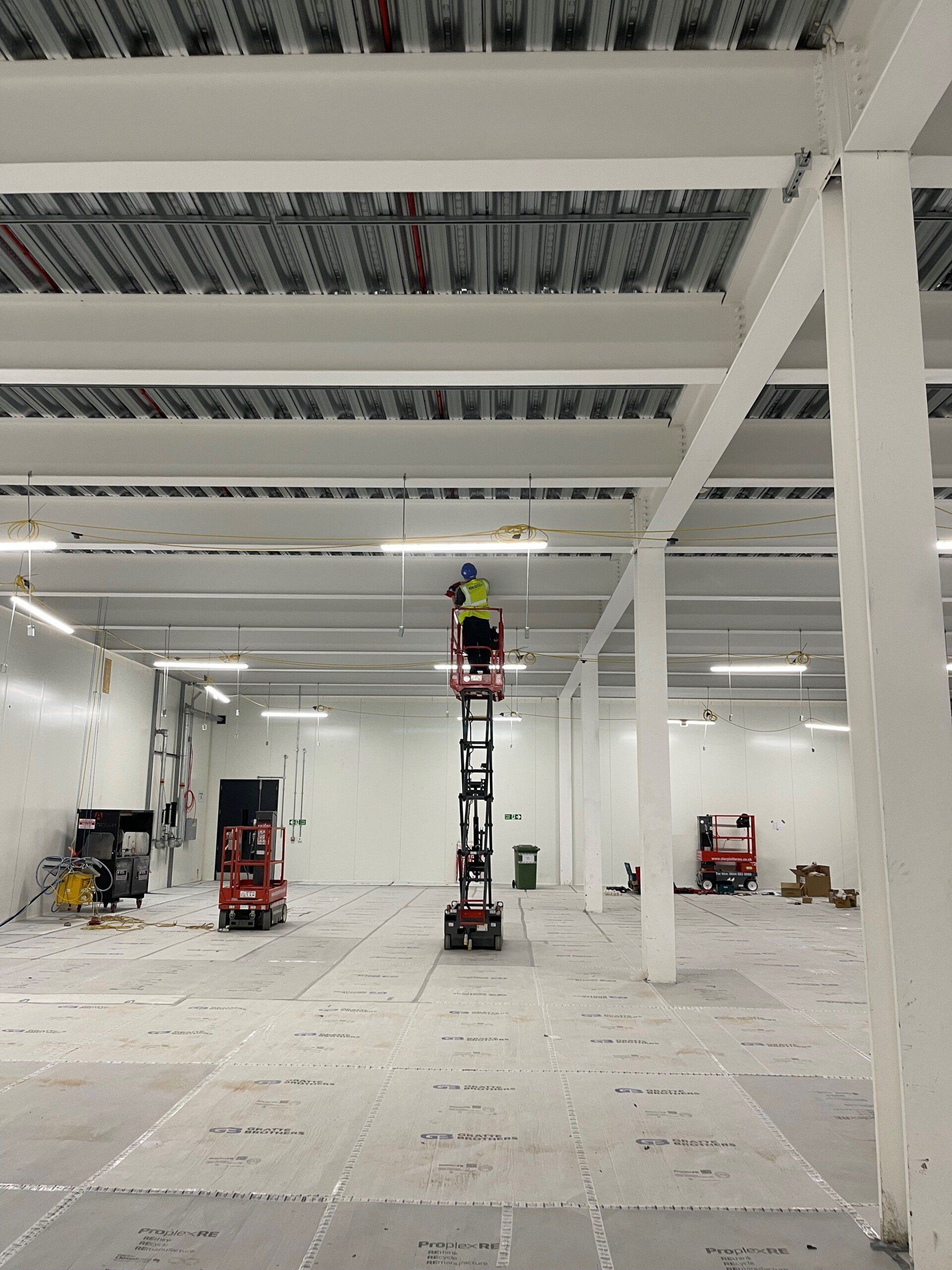 A man is standing on a lift in an empty warehouse.