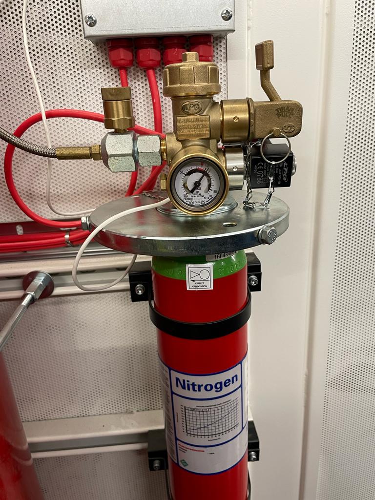 A red nitrogen cylinder with a gauge attached to it is hanging on a wall.