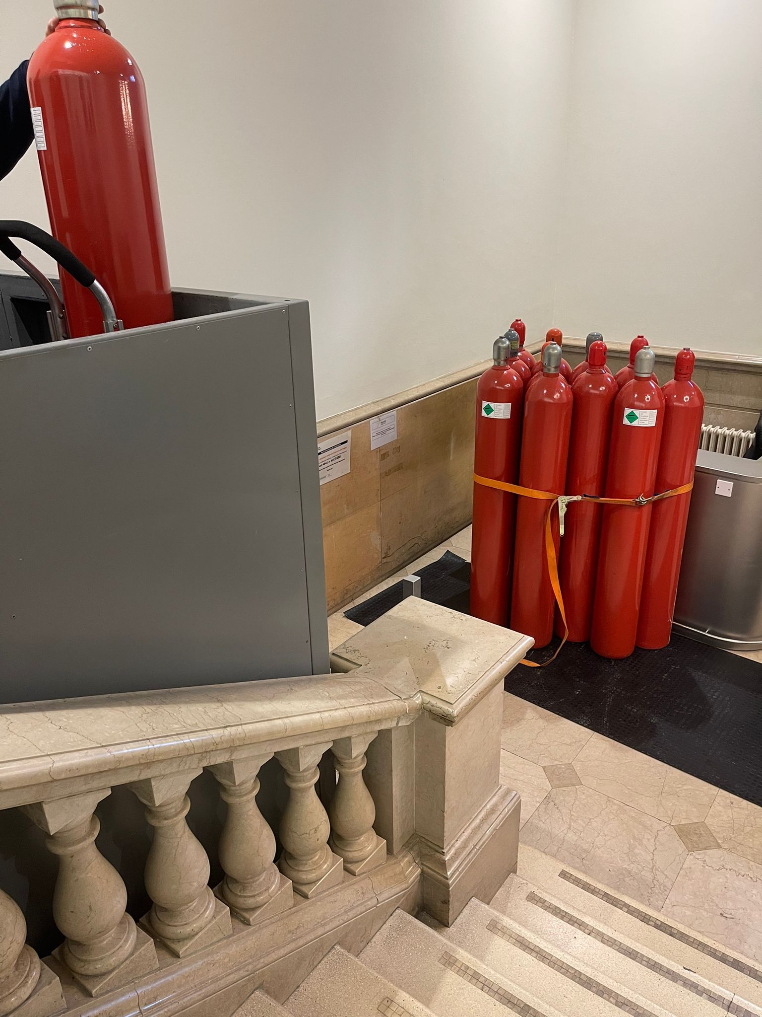 A fire extinguisher is sitting on top of a staircase next to a bunch of red cylinders.