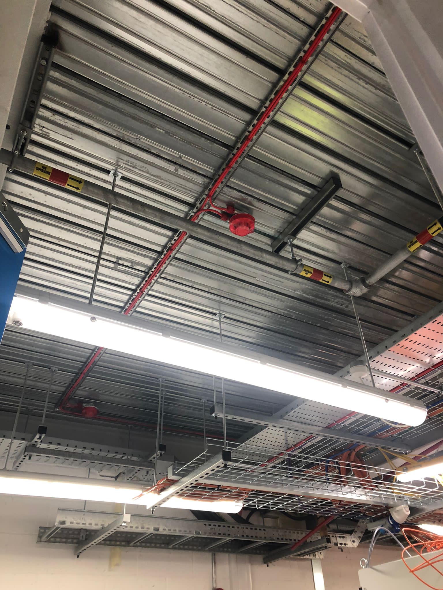 A ceiling with a lot of pipes and lights hanging from it.