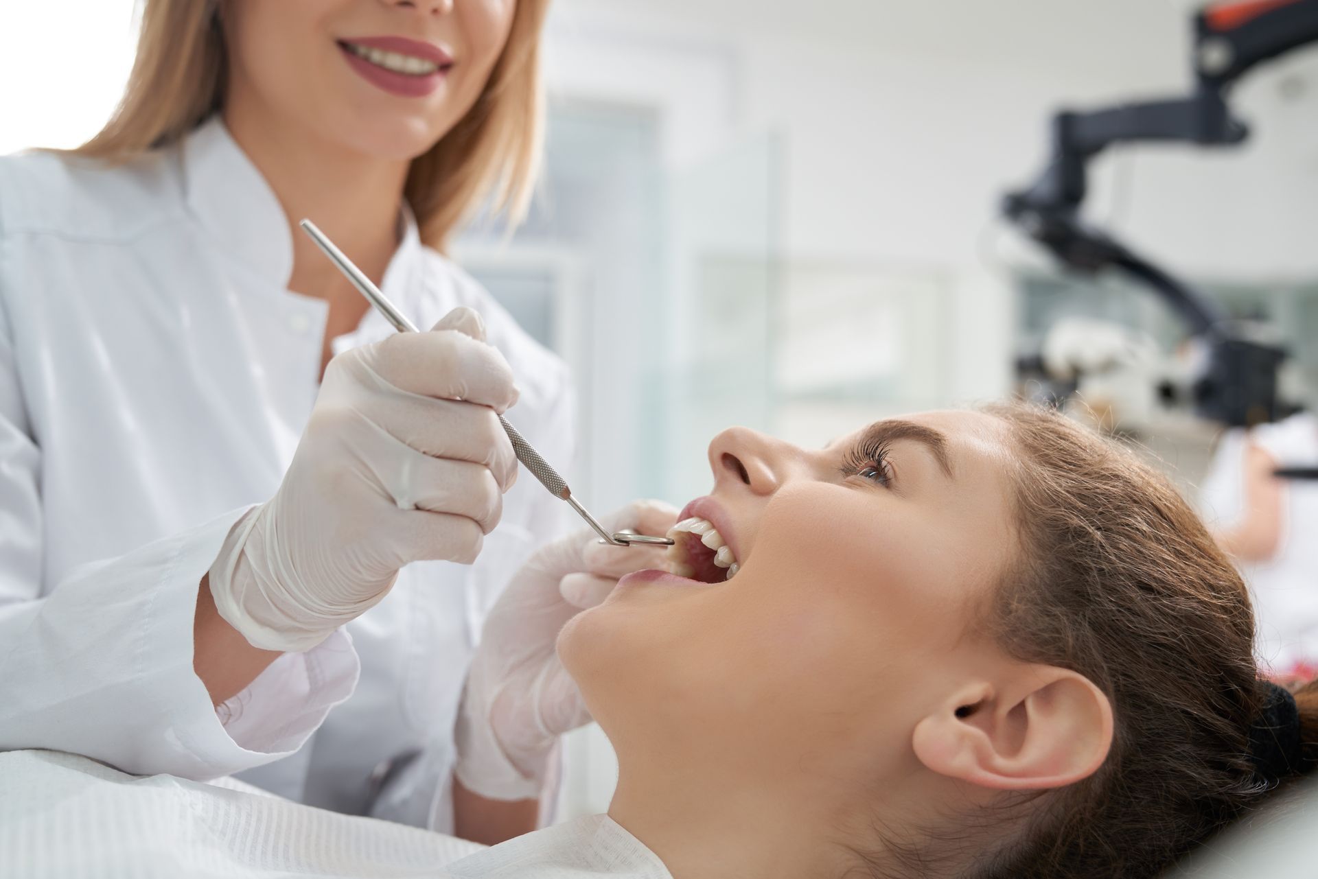Dentist examining a patient's teeth. Both are in a dental office setting.