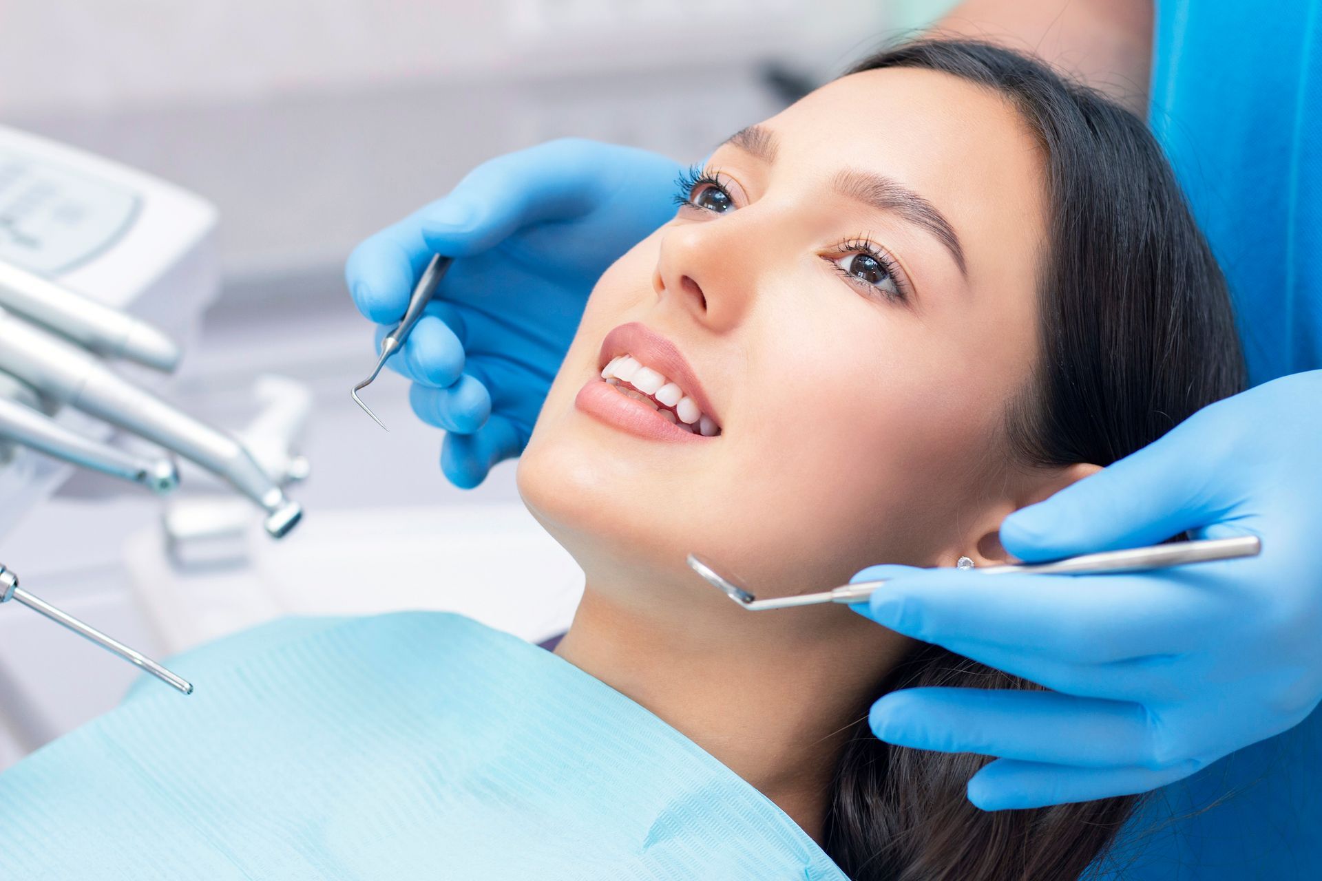 Dentist examining a smiling patient's teeth in a dental chair, wearing mask and gloves.