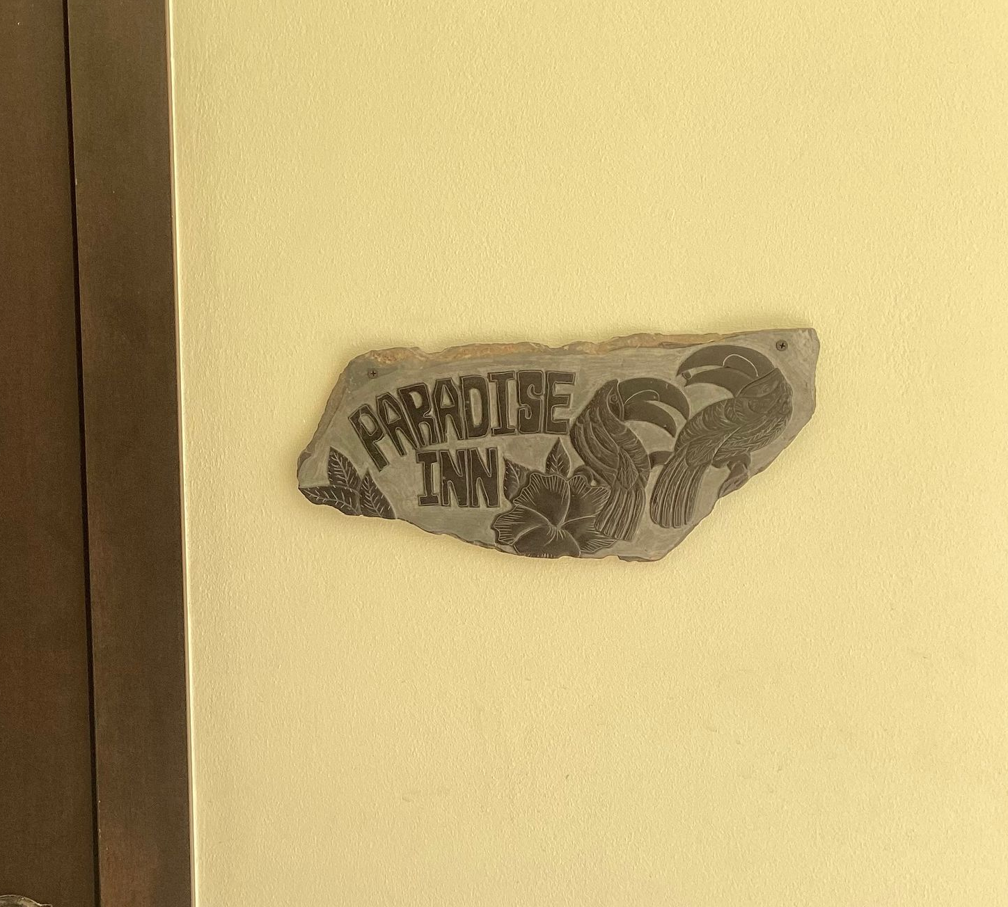 Small torn sticker on a beige wall beside a brown doorframe, reading “PARADISE INN.”