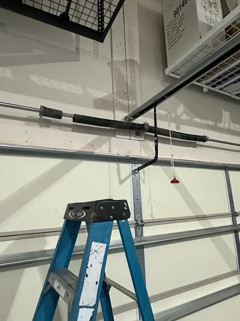 Blue ladder in a garage beneath a ceiling-mounted garage door opener and hanging cord.