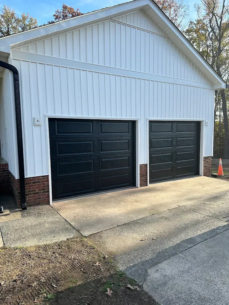 White garage with two black doors and brick trim on a concrete driveway