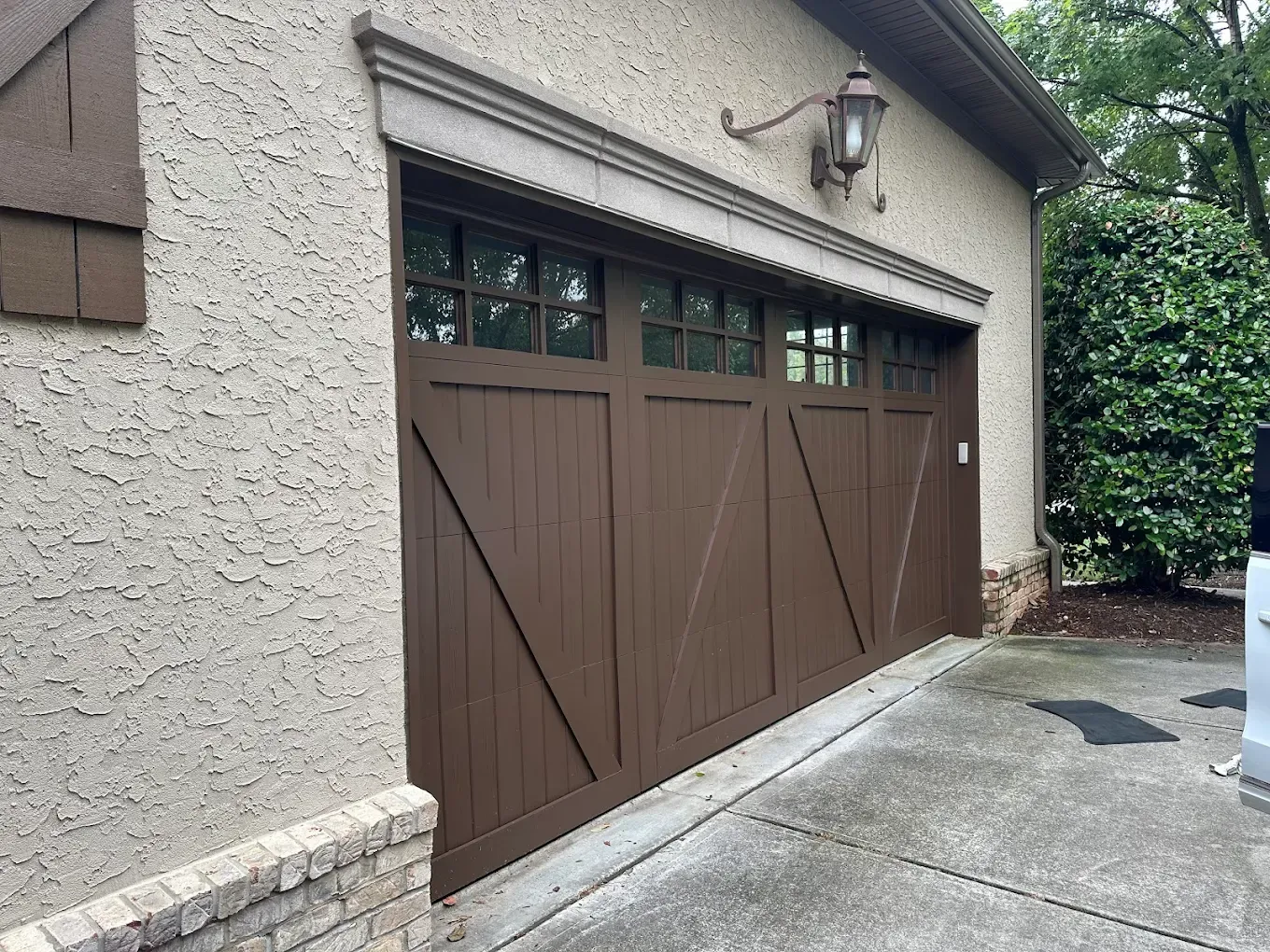 Brown garage door on a stucco house beside a sloped concrete driveway