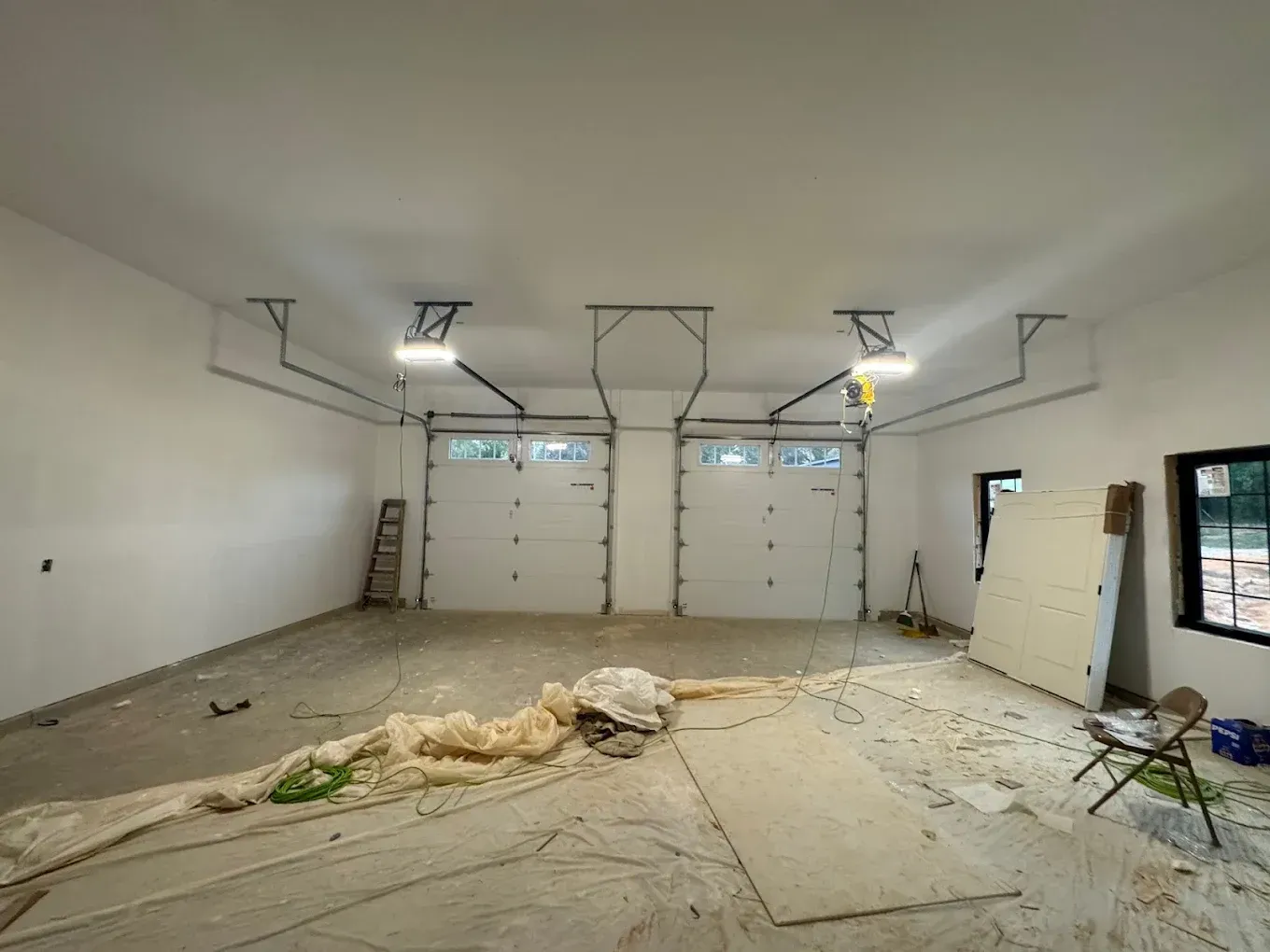 Unfinished garage interior with drywall debris, ladders, and open garage doors under construction.