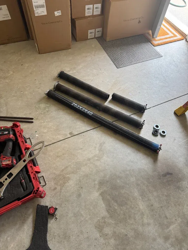 Garage floor with black metal parts, a red tool bag, cardboard boxes, and a small mat near a door.
