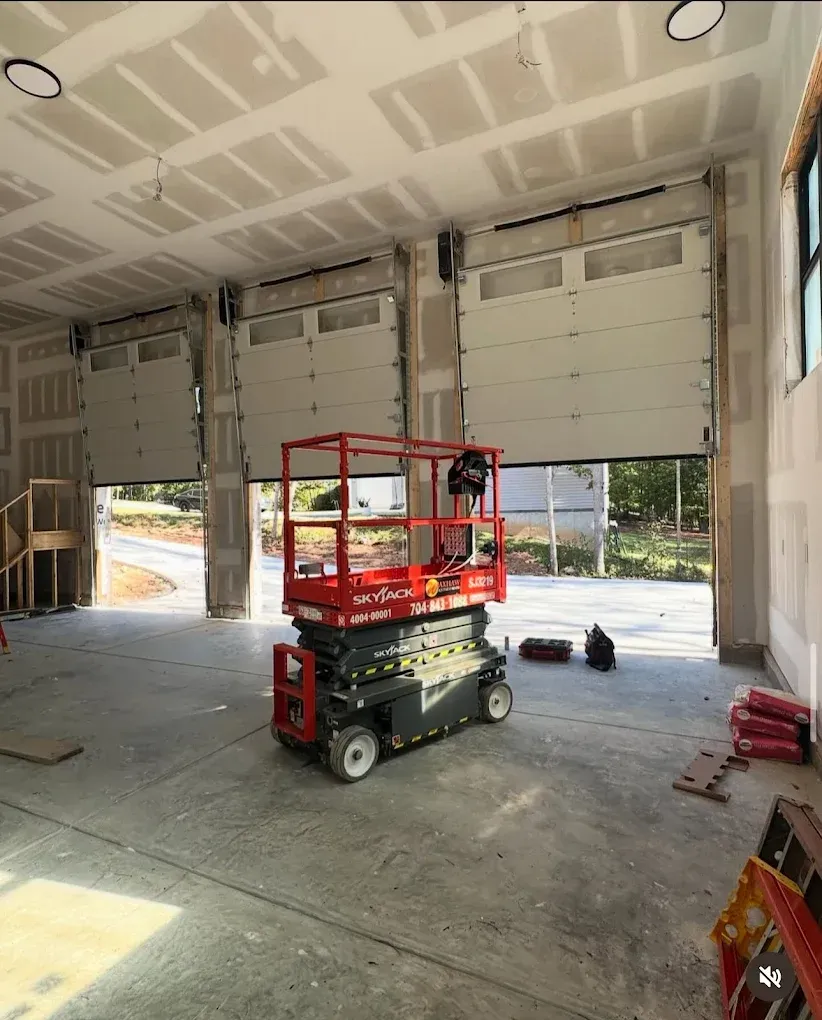 Red scissor lift inside an unfinished garage with open bay doors and concrete floor