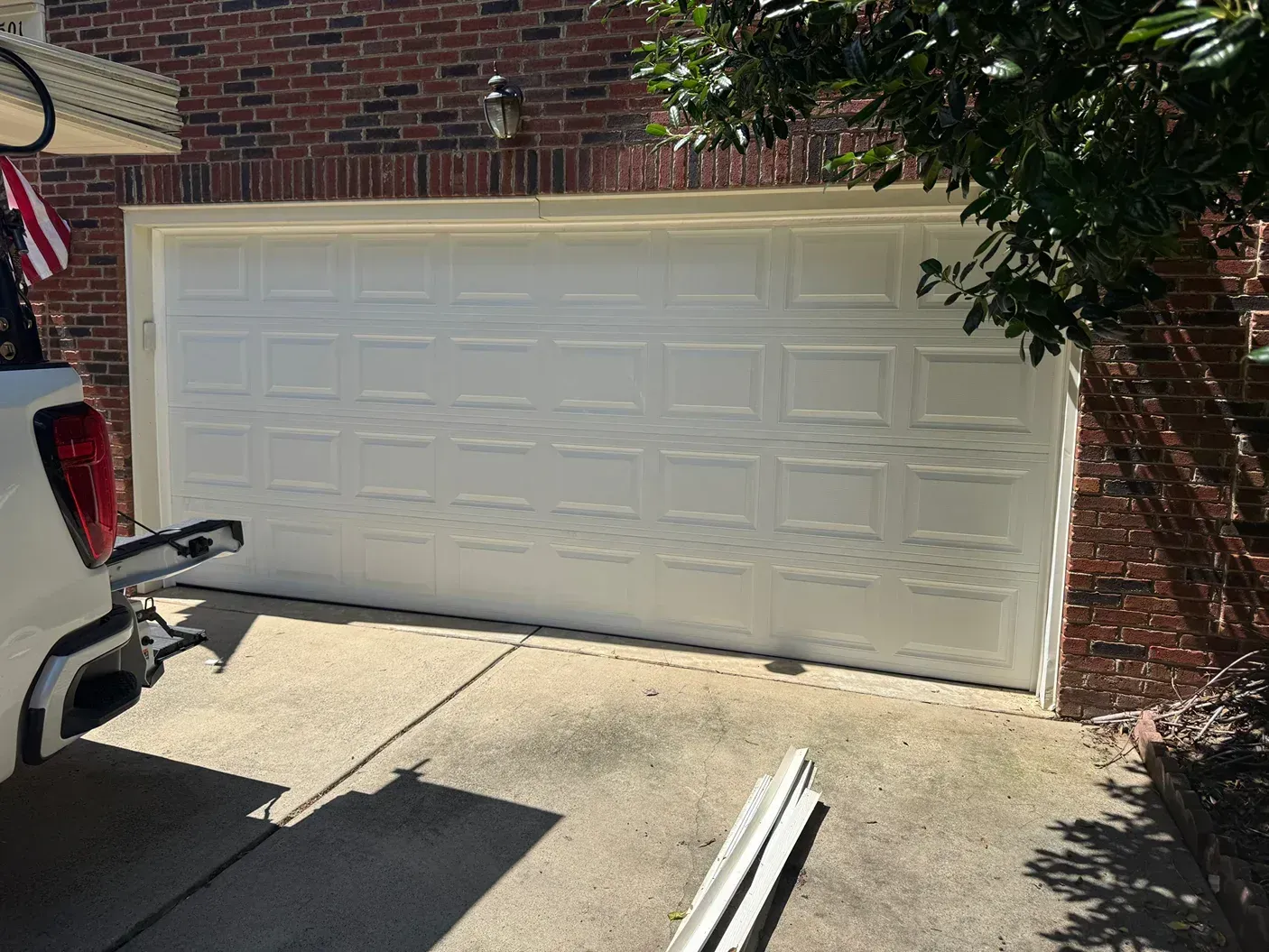 White double garage door on a brick house driveway, with a vehicle and trailer hitch visible on the left.