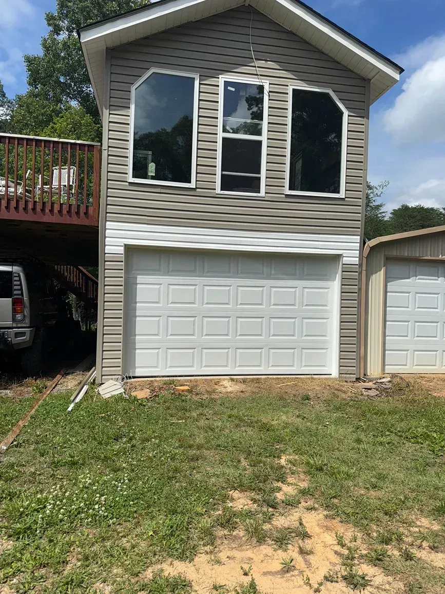 Two-story gray garage with white trim, large upper windows, and a white roll-up door beside a deck.