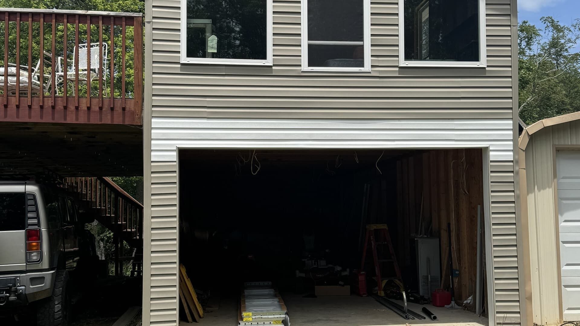 House exterior with open garage; a vehicle is parked on the left under a wooden deck.