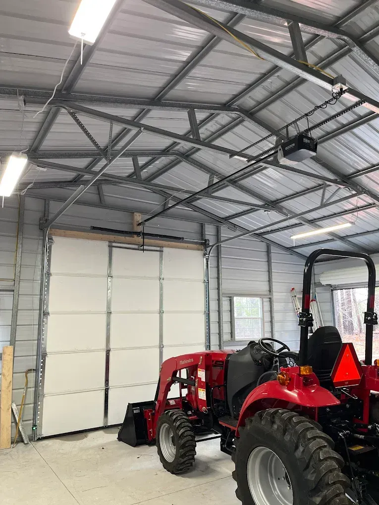 Red tractor parked inside a metal garage with large white overhead doors