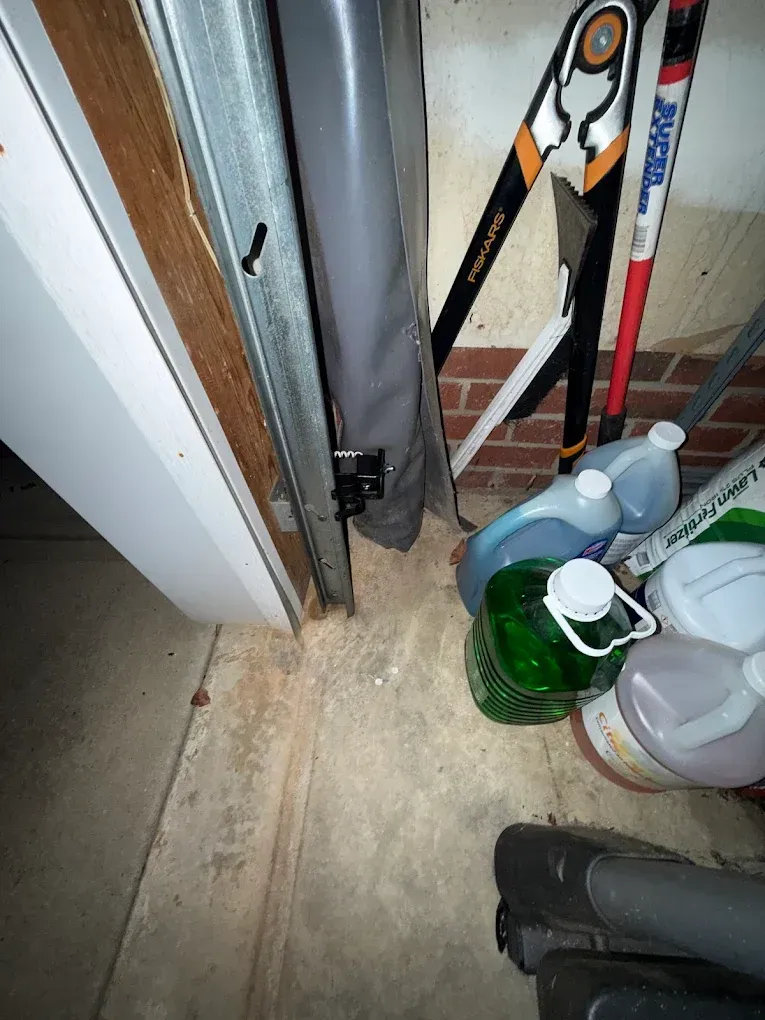 Cluttered storage area with cleaning supplies, tools, and pipes beside a doorframe.