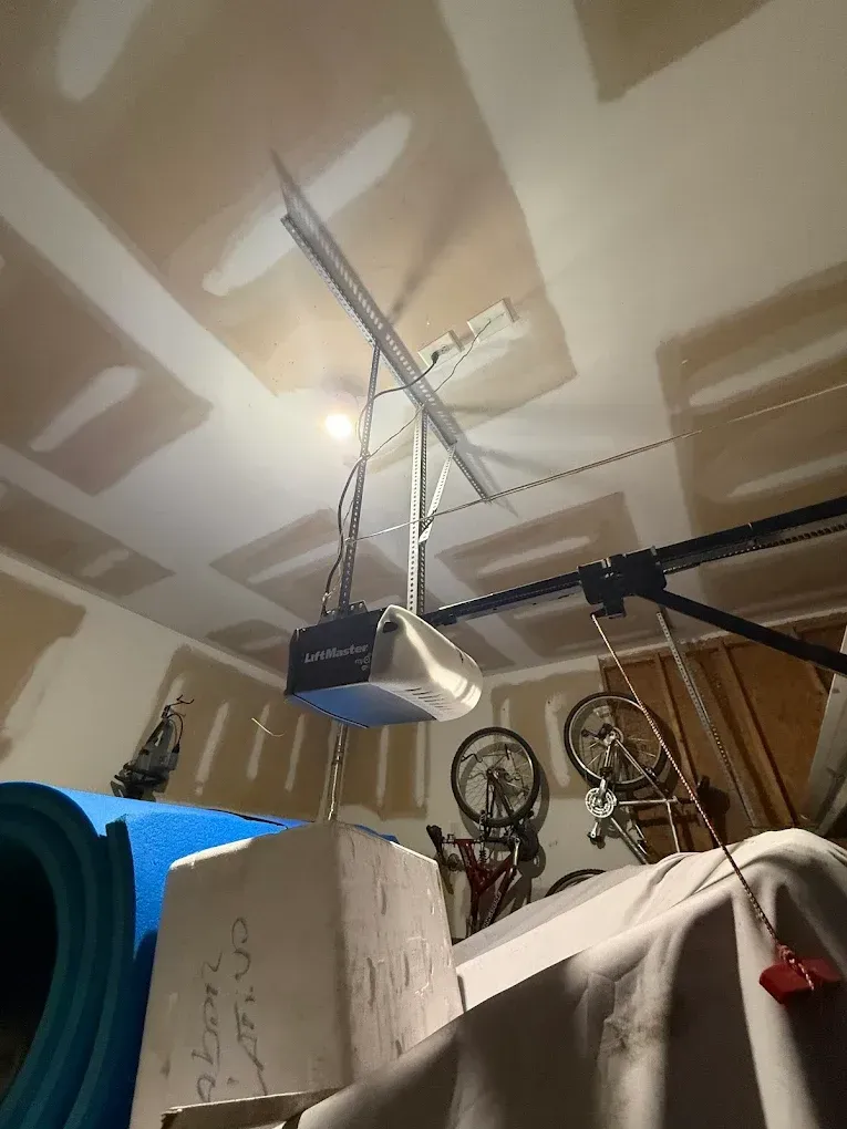 Garage ceiling with a pulley hoist lifting a black device, surrounded by stored items and bicycles.